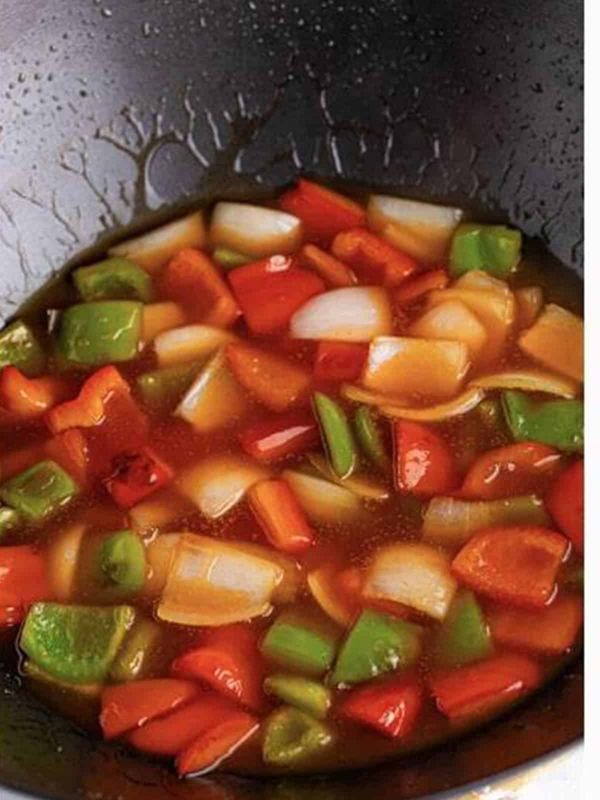 Thickened sweet and sour sauce simmering with bell peppers and onion in a wok.