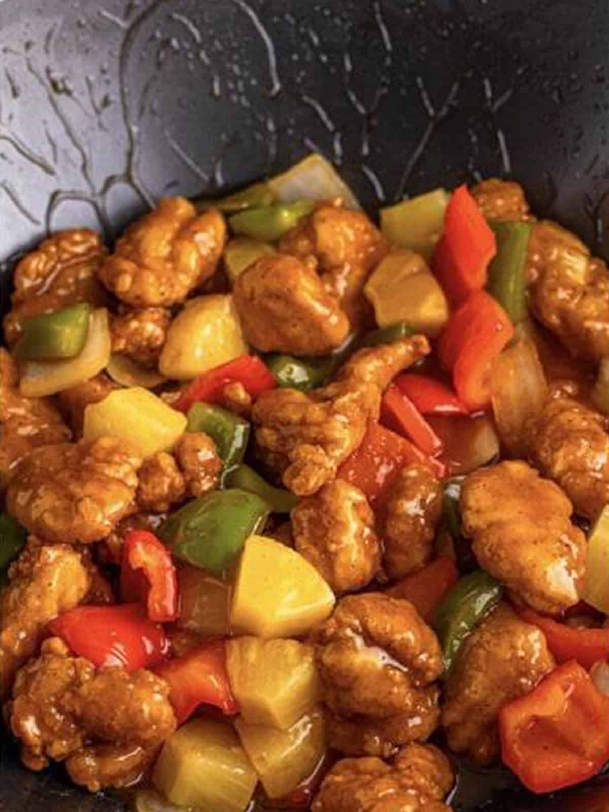 Finished sweet and sour chicken tossed in glossy sauce with peppers and pineapple.