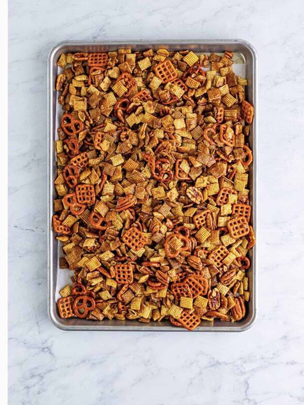 Coated Sweet Chex Mix spread on a sheet tray ready to bake.