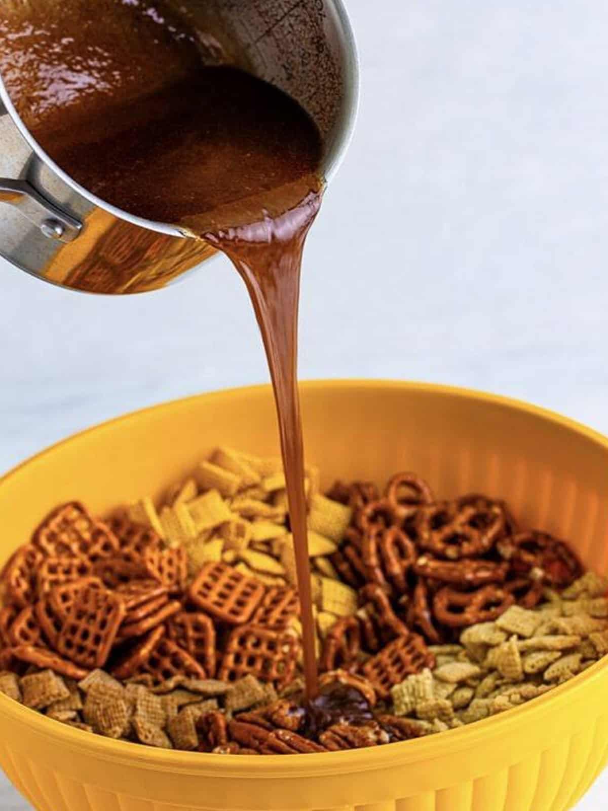 Pouring the cinnamon sugar butter sauce over the Chex mix to coat it.