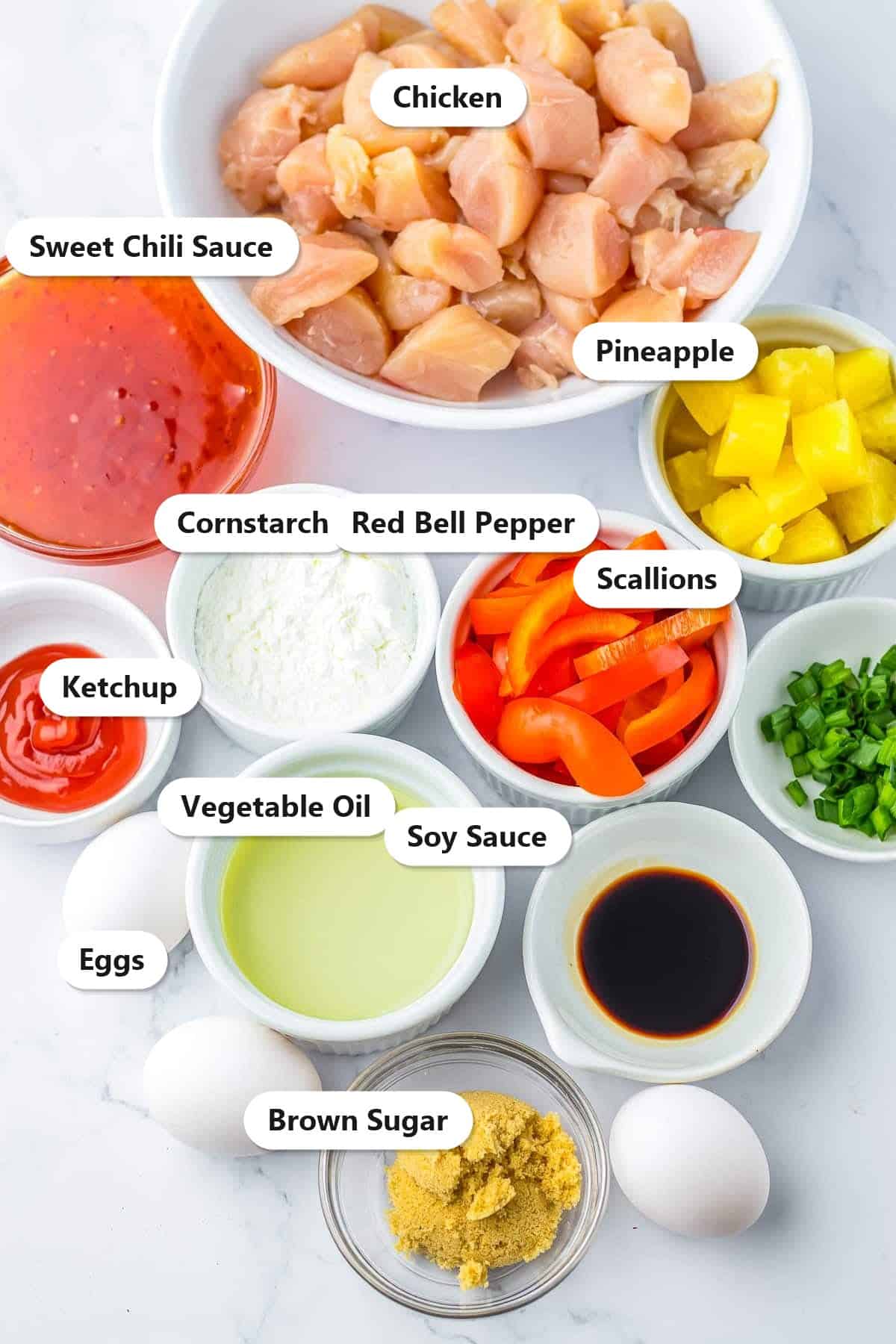 Labeled ingredients to make sweet chili chicken including chicken, sweet chili sauce, pineapple, cornstarch, red bell pepper, scallions, soy sauce, and eggs.