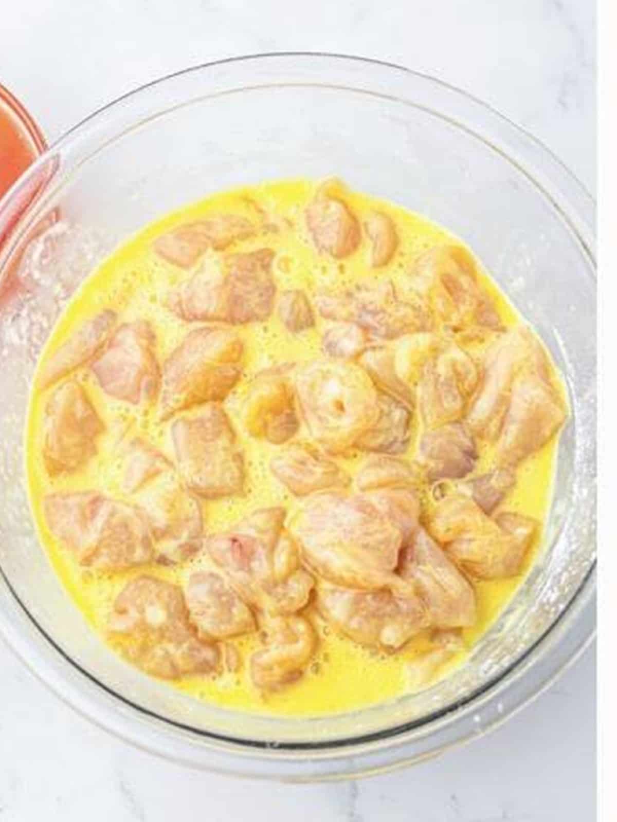 Bite-sized chicken pieces coated in a beaten egg and cornstarch mixture in a bowl.