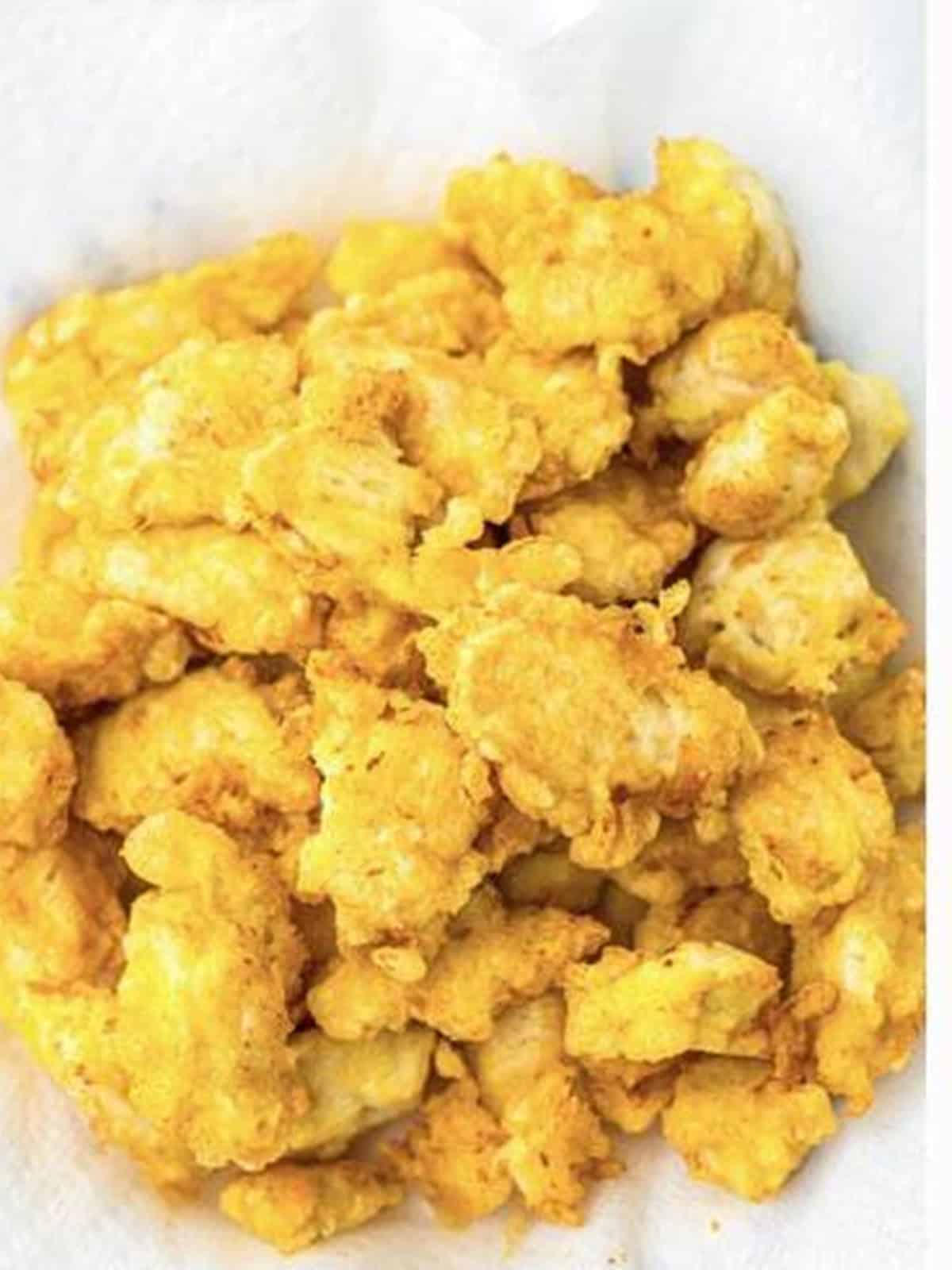 Golden fried chicken pieces draining on a paper-towel-lined plate.