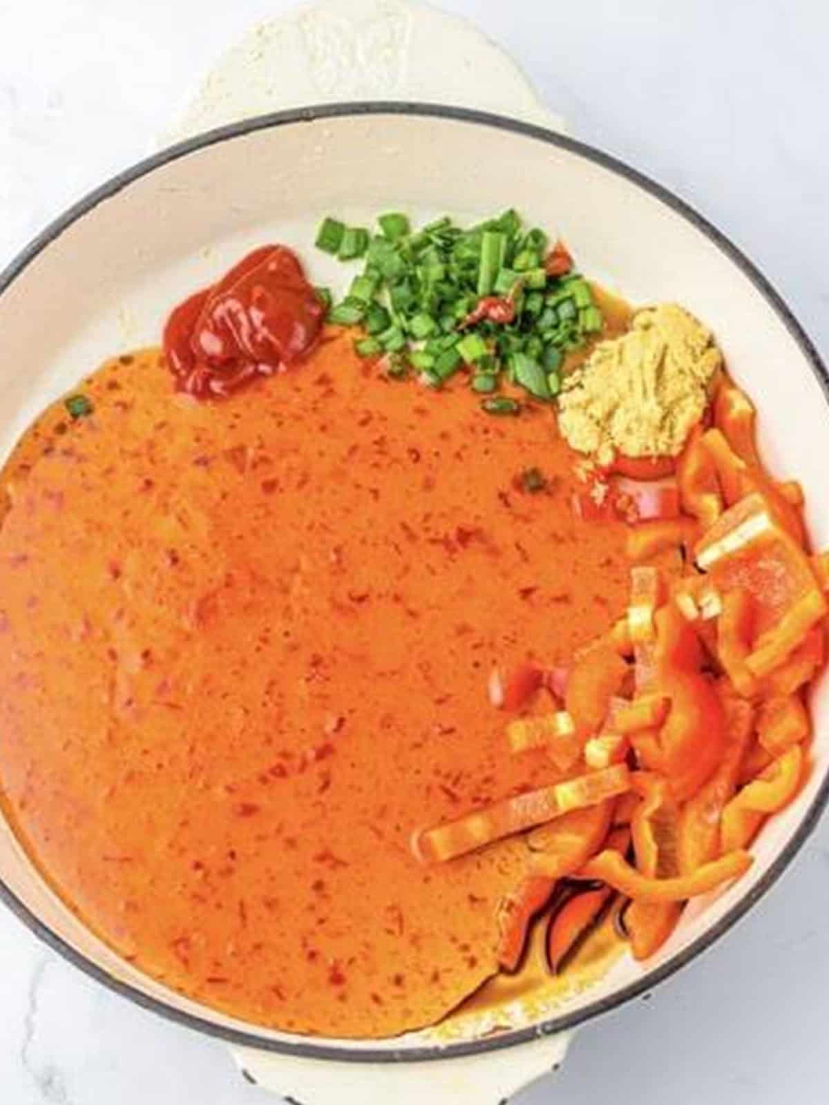 Sweet chili sauce with ketchup, scallions, and bell pepper coming together in a skillet.