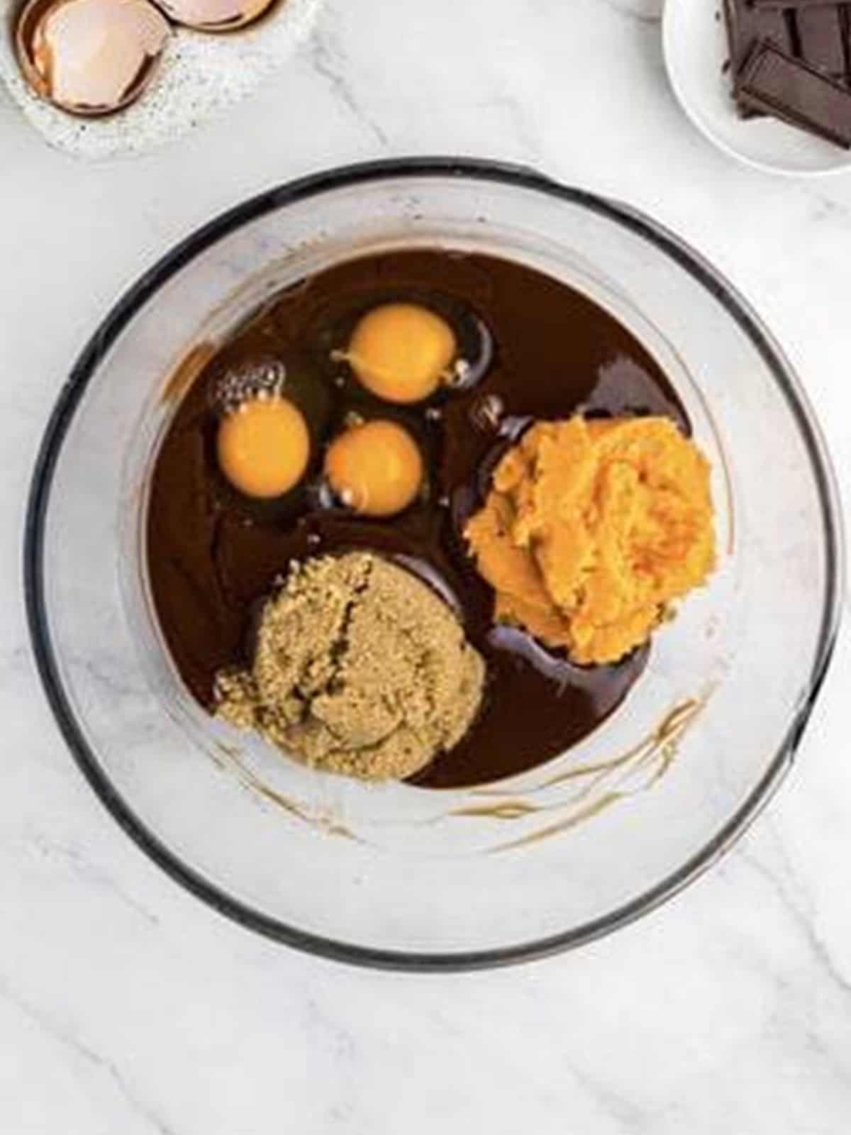 Sweet potato puree, eggs, and brown sugar added to melted chocolate in a bowl.