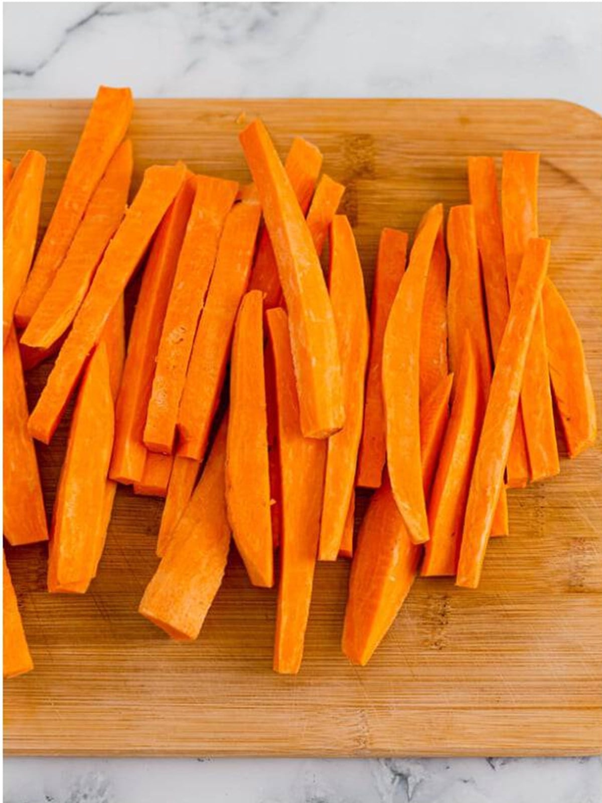 Sweet potatoes cut into even sticks on a cutting board