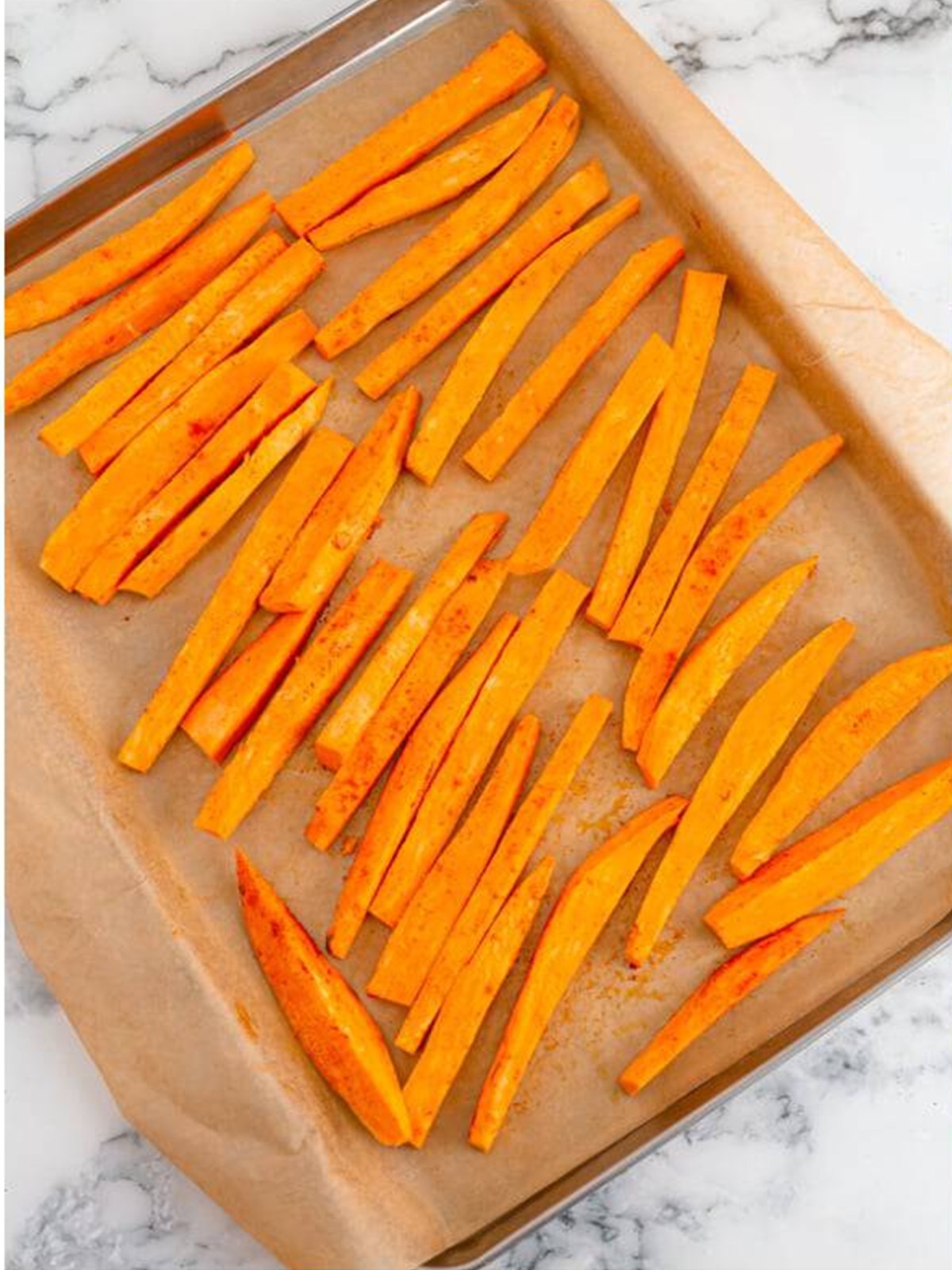 Seasoned sweet potato fries in a single layer on a sheet pan