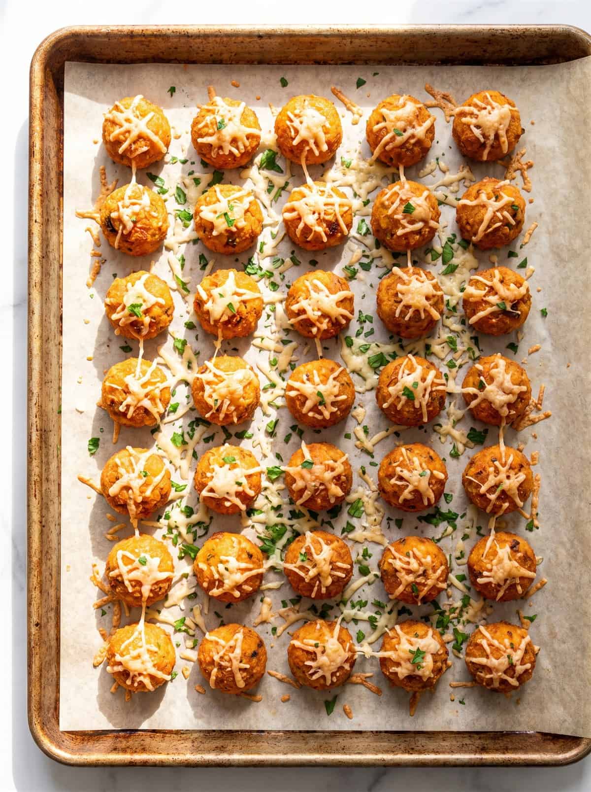 Golden baked sweet potato tots on a parchment-lined baking sheet.