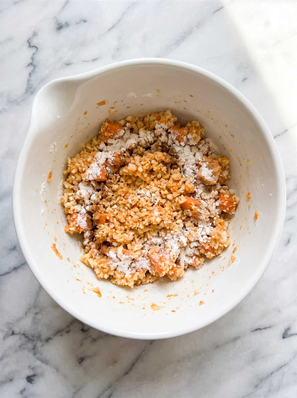 Riced sweet potato and cauliflower mixed with flour and seasonings in a bowl.