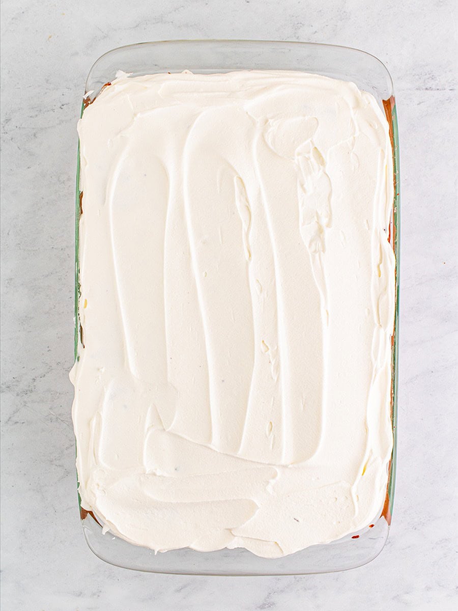 Top layer of cool whip smoothed over the swiss roll lush cake.