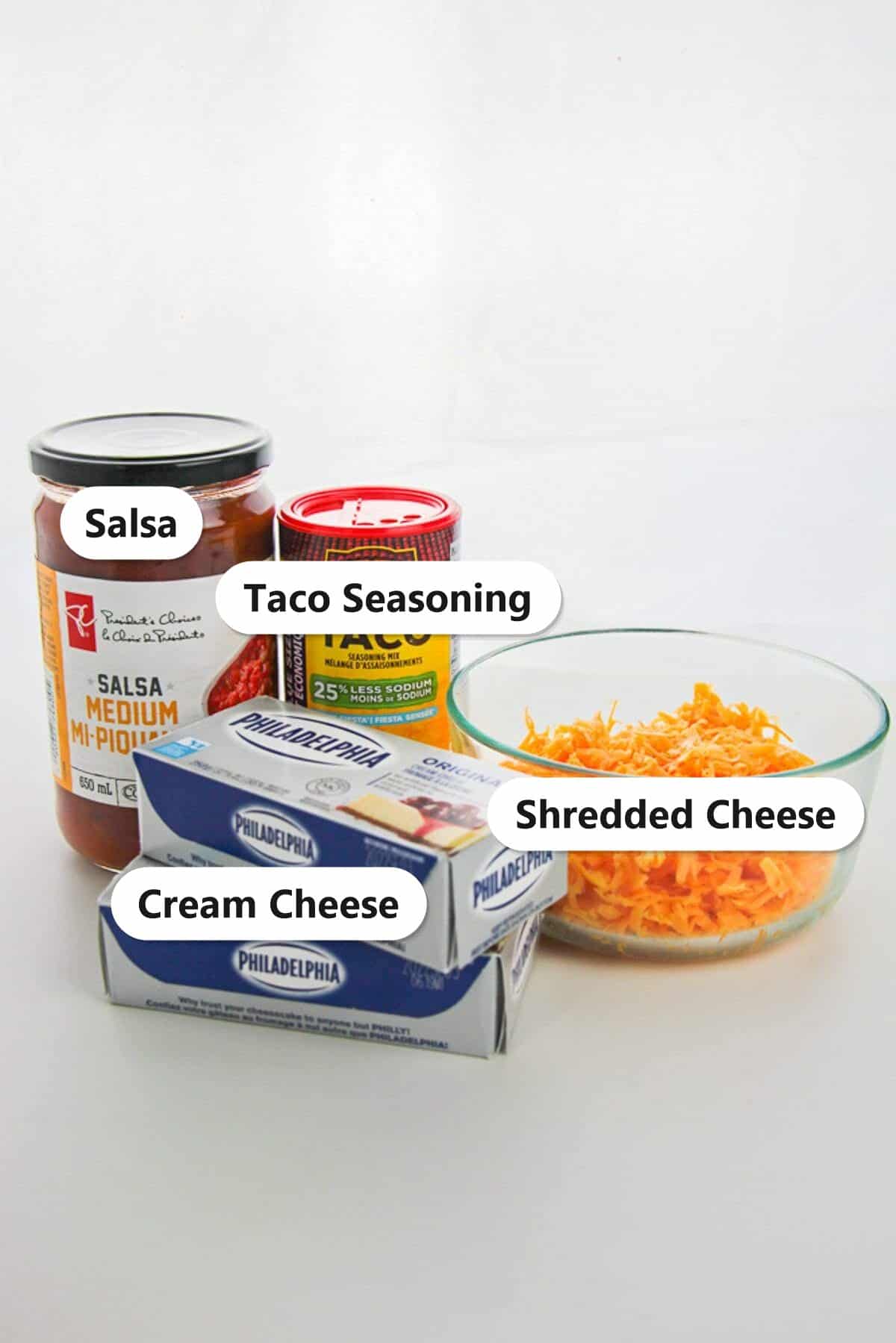 Labeled ingredients to make taco dip including salsa, taco seasoning, cream cheese, and shredded cheese.