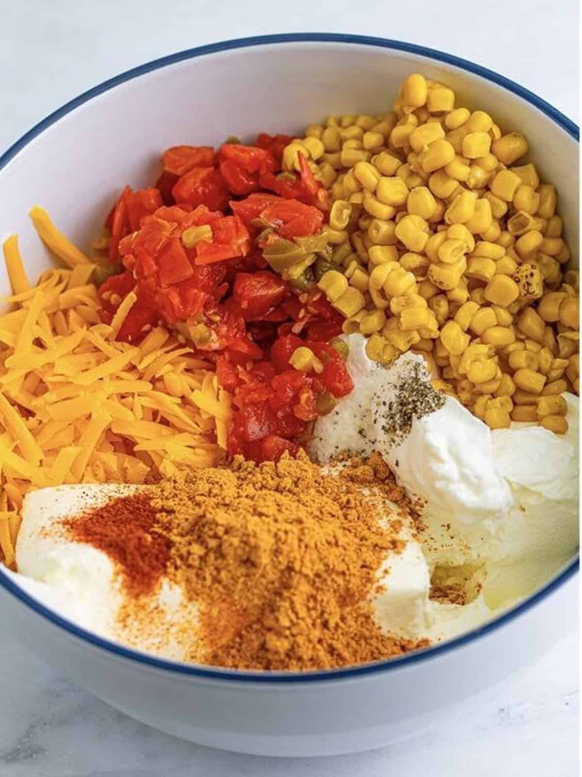 Cheddar, cream cheese, sour cream, corn, Rotel, and taco seasoning added to a large bowl to make taco dip.