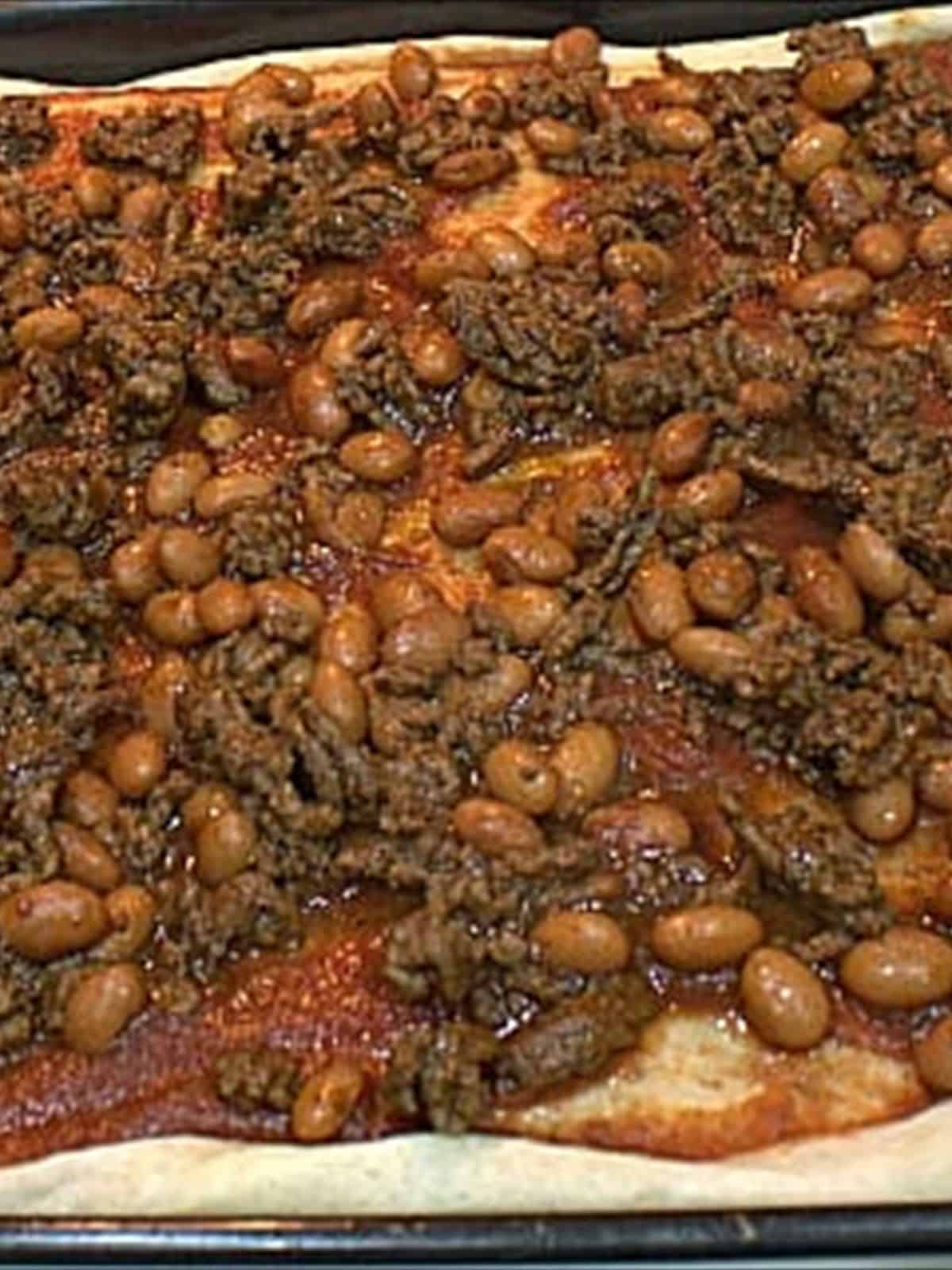 Taco sauce and seasoned beef and beans spread over the pre-baked pizza crust.
