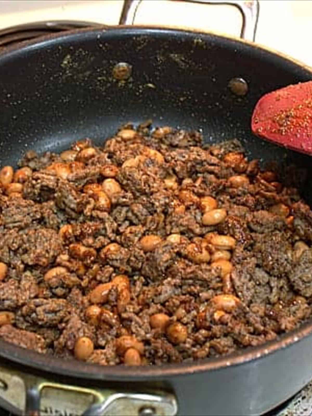 Ground beef browned with taco seasoning and pinto beans in a skillet for taco pizza.