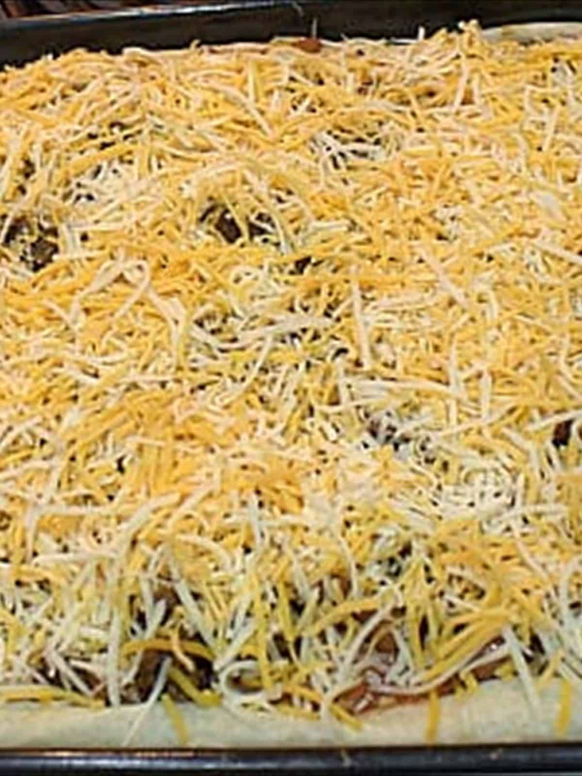 Shredded cheddar and Monterey Jack cheese sprinkled over the taco pizza toppings.