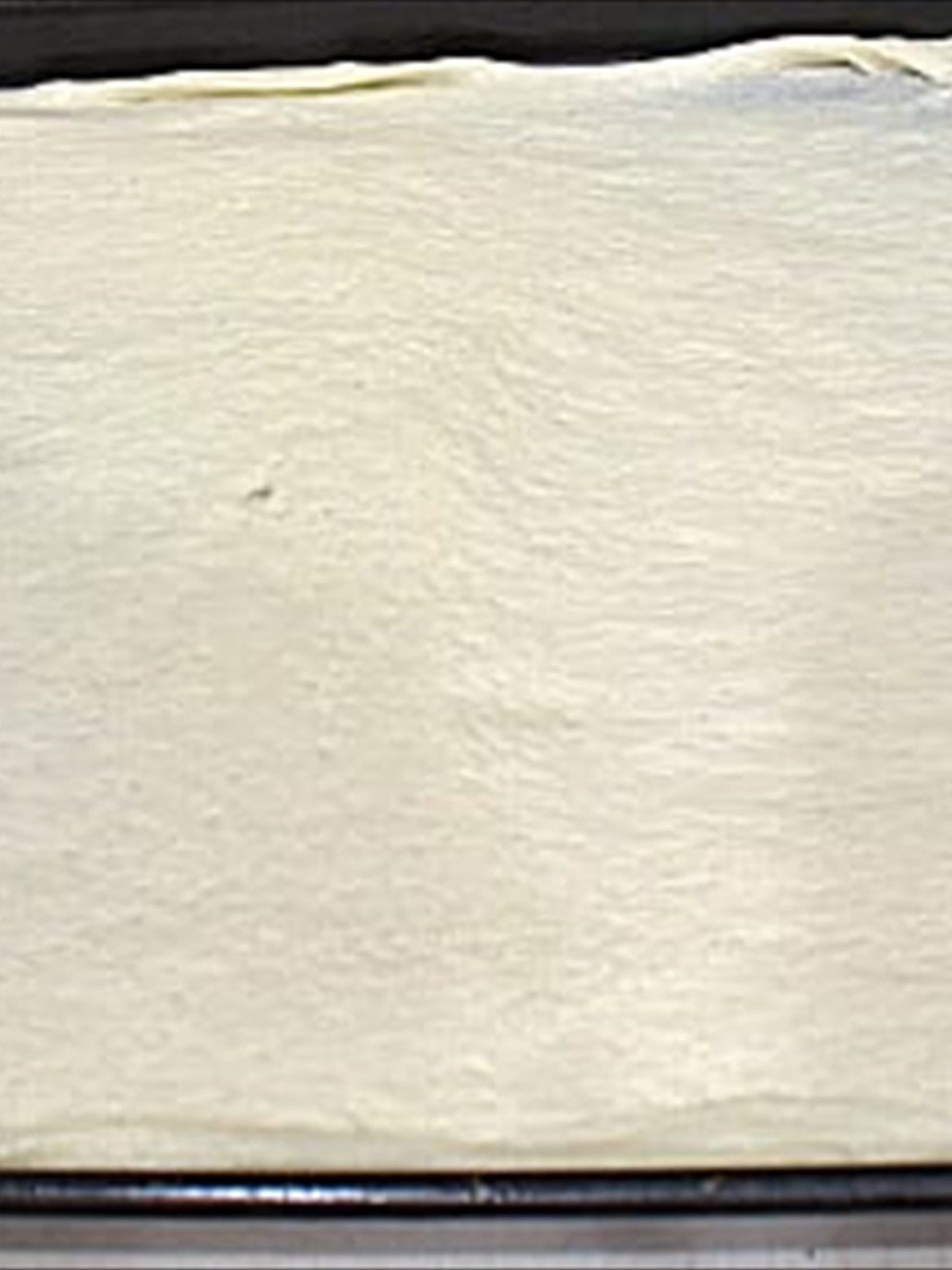 A thin pizza crust pressed onto a baking sheet for taco pizza.