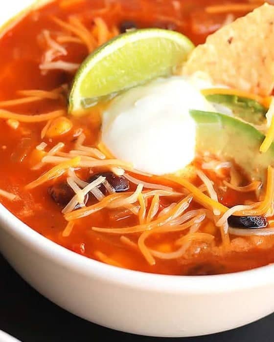 A close-up of Taco Soup topped with cheese, sour cream, lime, and avocado.