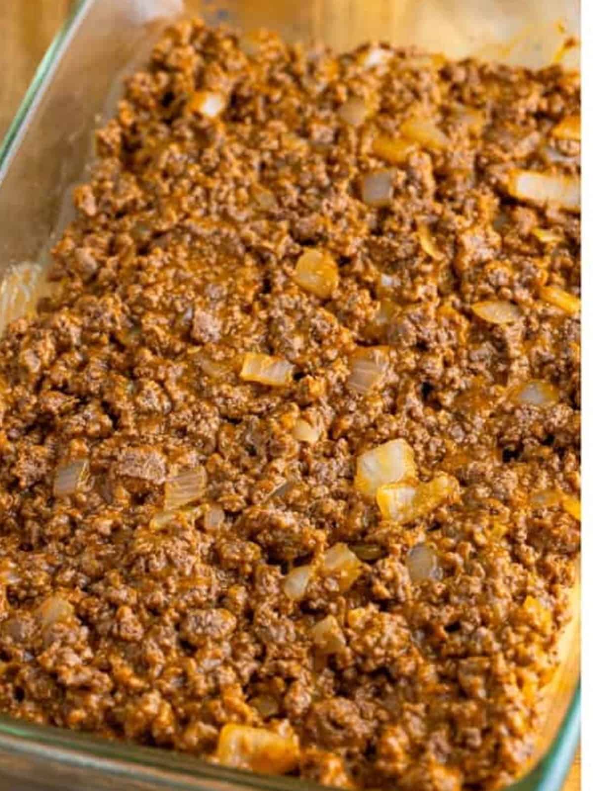 Seasoned ground beef and cheddar soup mixture spread in a baking dish for tater tot casserole.
