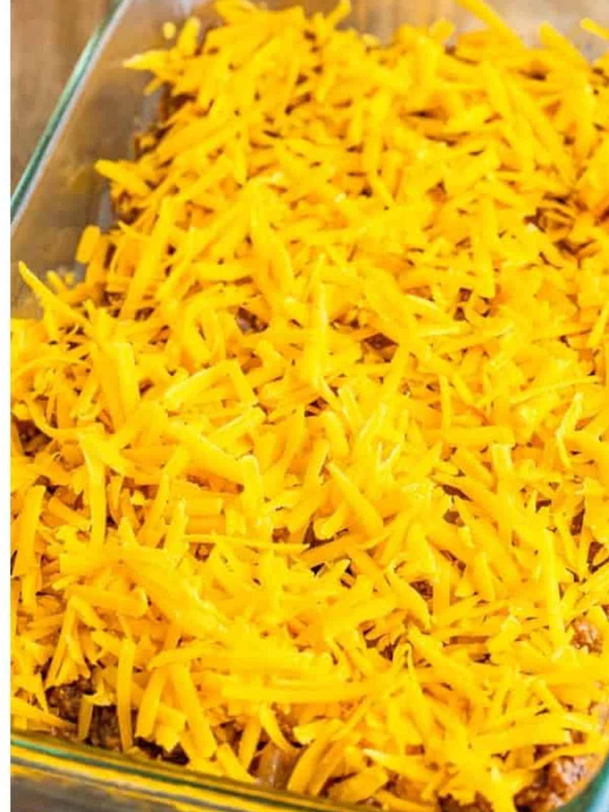 Shredded cheddar cheese sprinkled over the beef mixture for tater tot casserole.