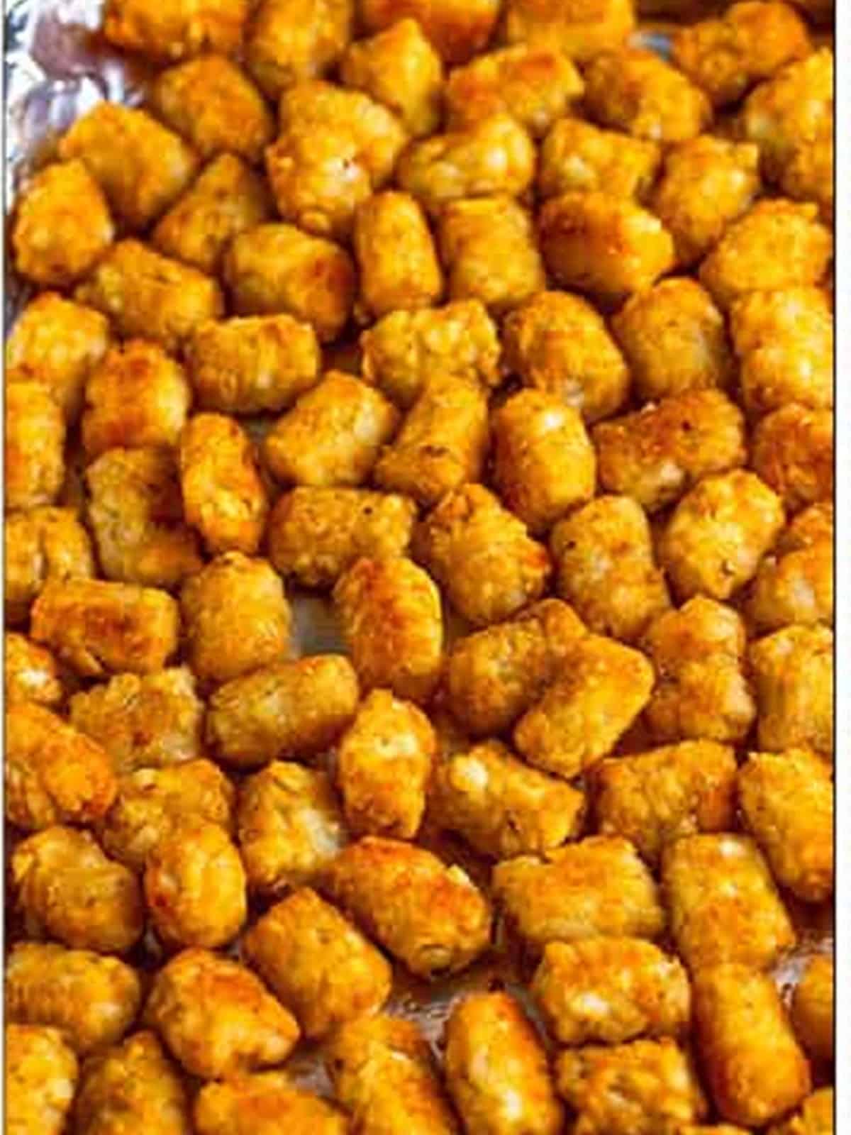 Baked tater tots spread on a foil-lined sheet for Tater Tot Nachos.