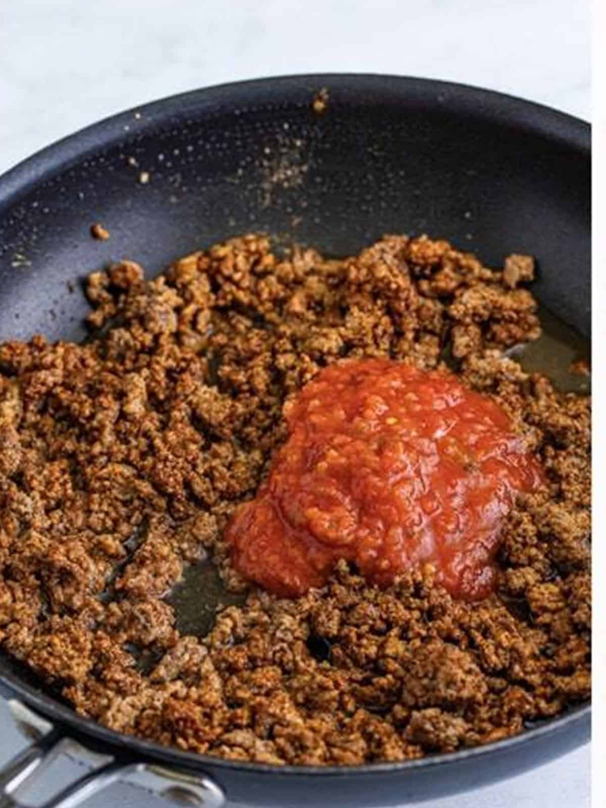 Salsa being added to seasoned taco meat in a skillet.