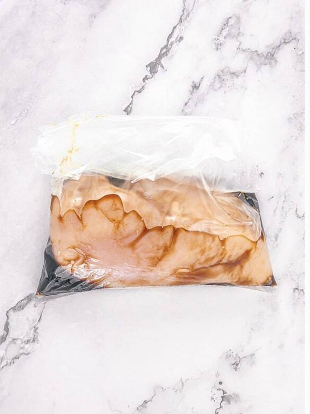 Chicken breast marinating in teriyaki sauce in a bag.