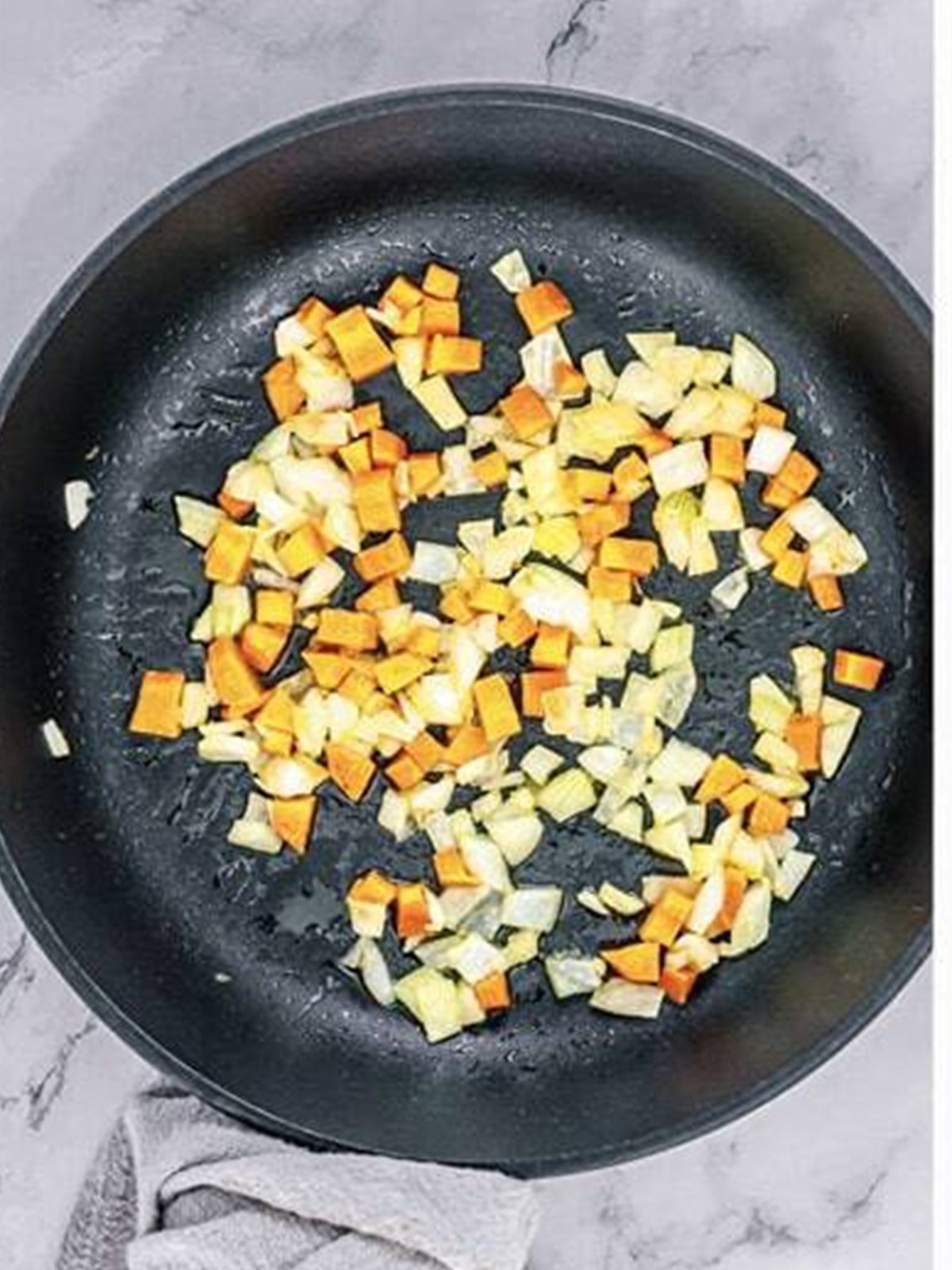 Diced carrot and onion sauteing in a hot skillet for teriyaki chicken fried rice.