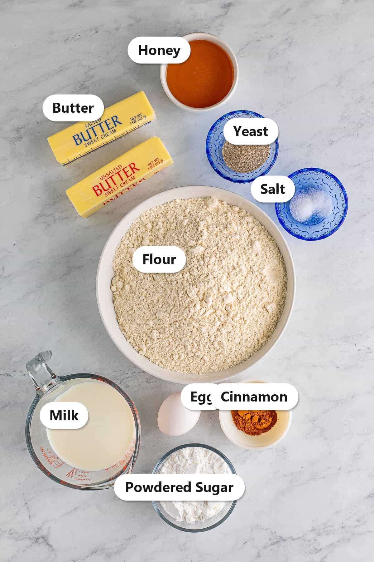 Labeled ingredients for Texas Roadhouse rolls including flour, milk, butter, honey, yeast, egg, salt, cinnamon, and powdered sugar.
