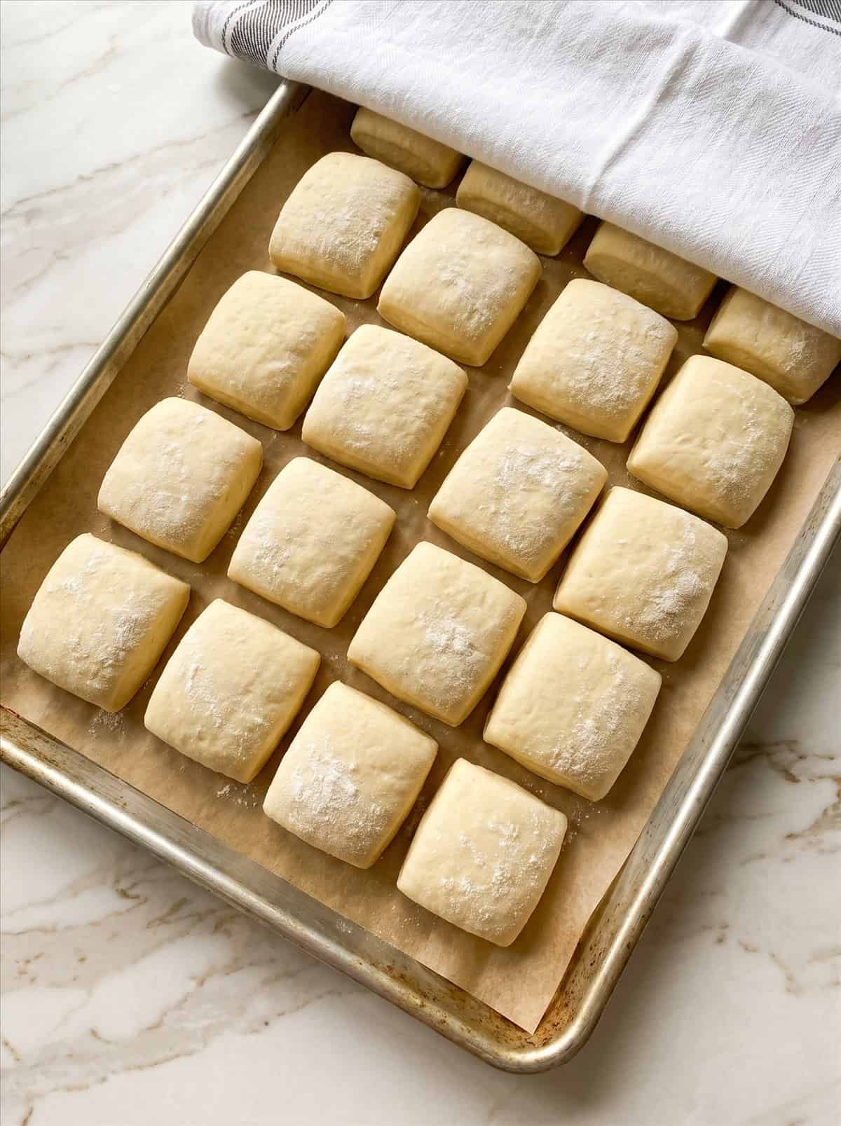 Soft dough cut into squares and risen on a parchment-lined baking sheet.