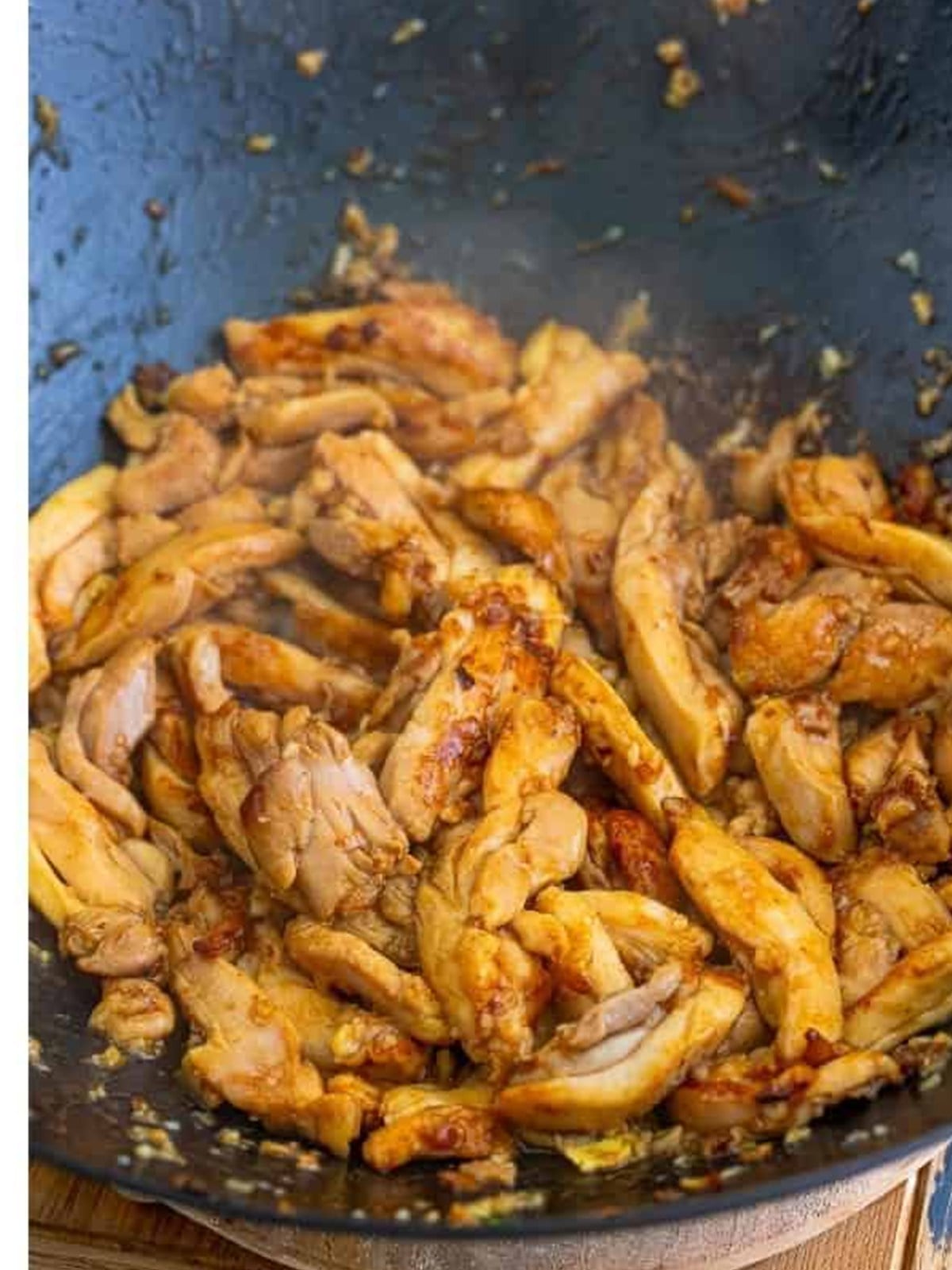 Sliced chicken thighs seared in a wok for pad see ew.