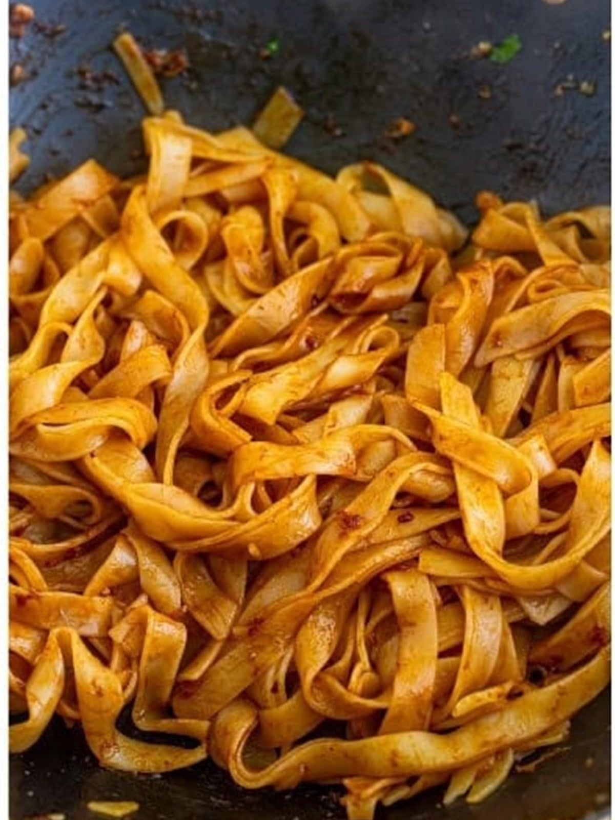 Wide rice noodles tossed in pad see ew sauce in a wok.