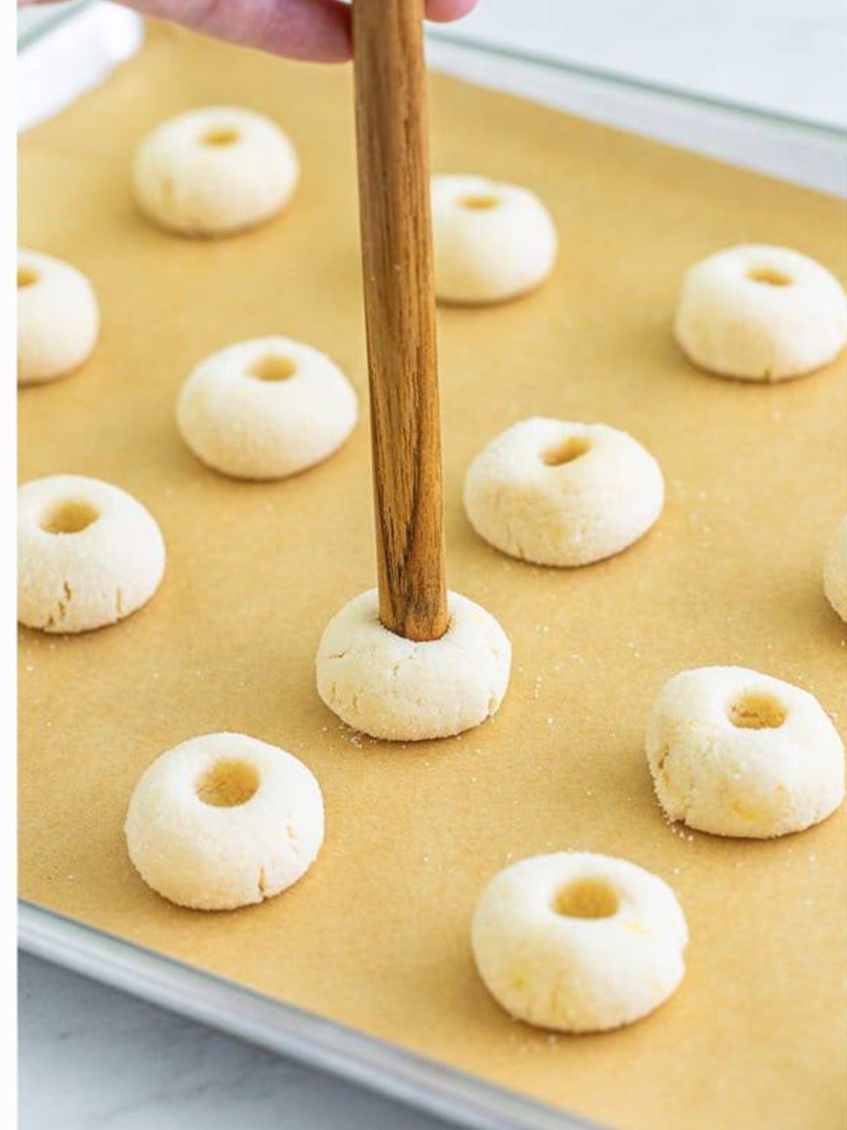 Pressing a thumbprint into each cookie dough ball with a wooden dowel on a baking sheet.