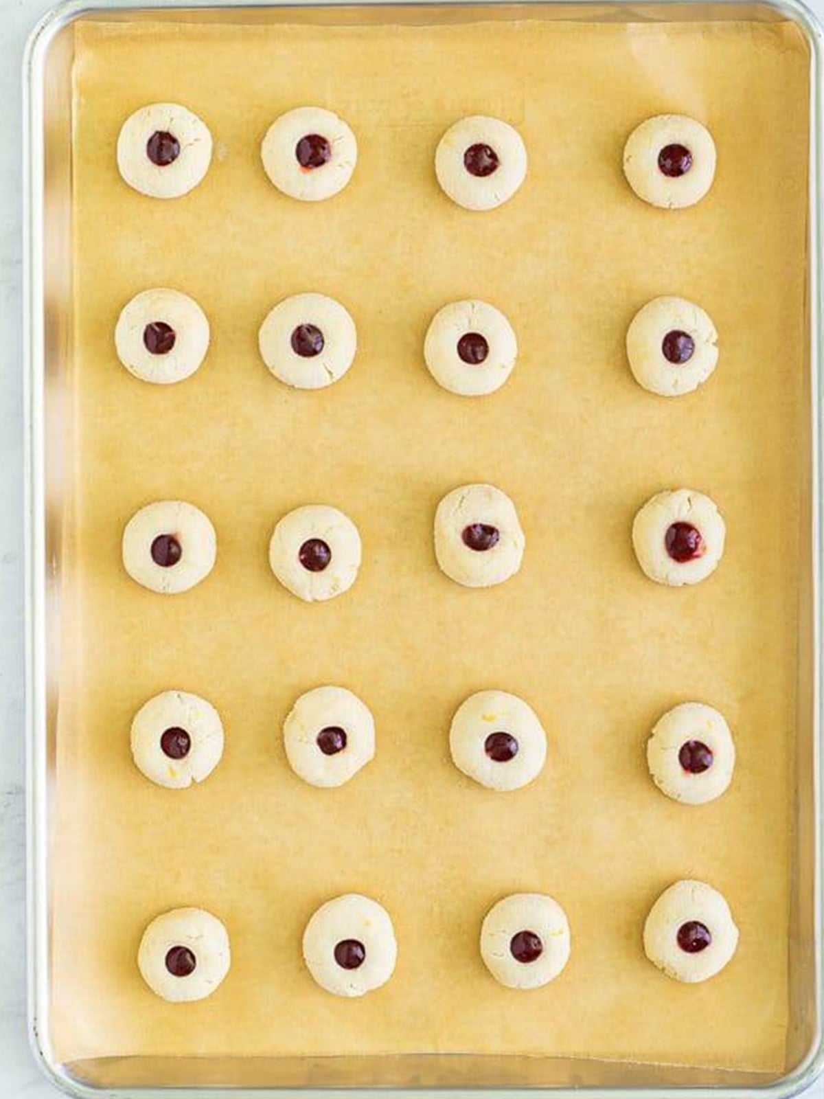 Thumbprint cookies filled with raspberry jam on a parchment lined baking sheet.