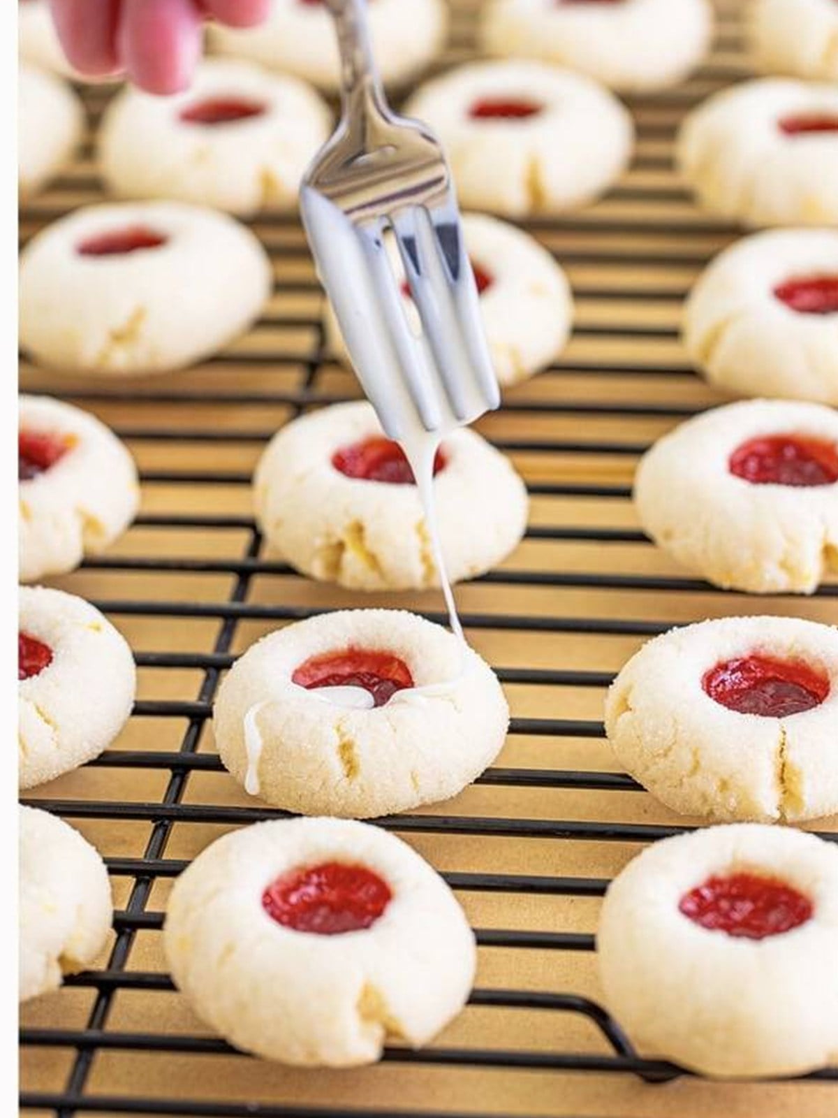 Lemon glaze drizzled over baked raspberry thumbprint cookies on a wire rack.