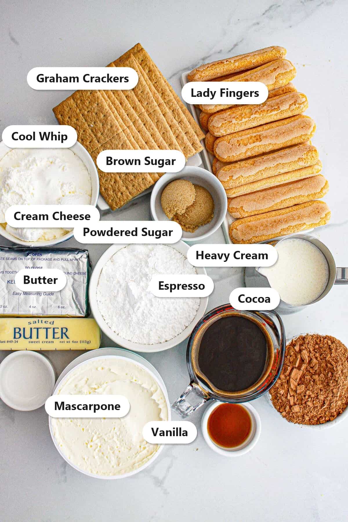 Labeled ingredients for tiramisu cheesecake including graham crackers, lady fingers, mascarpone, cream cheese, espresso, cocoa, cool whip, and heavy cream.