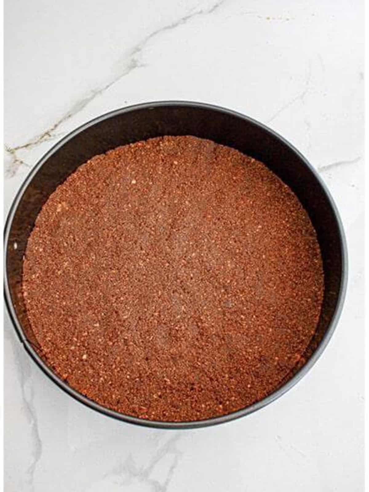 Chocolate graham cracker crust pressed into a springform pan for tiramisu cheesecake.