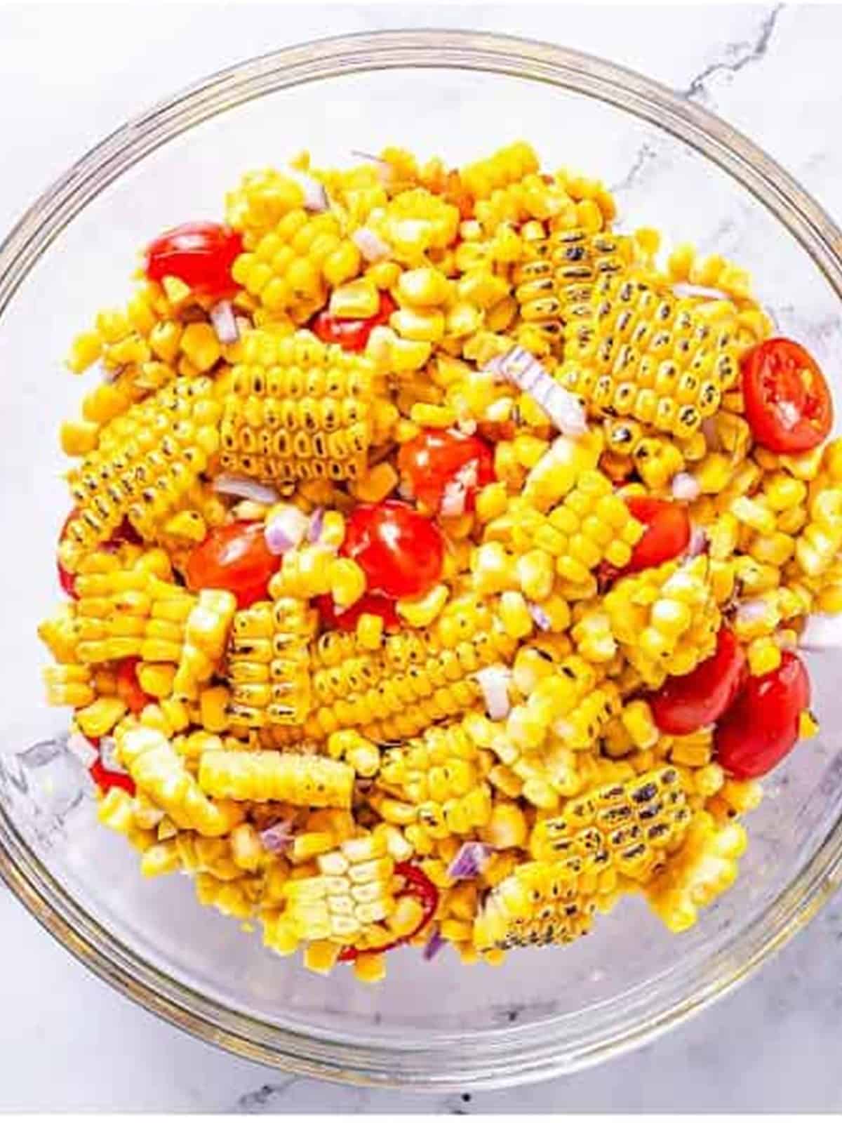 Grilled corn kernels added to grape tomatoes and red onion in a bowl.