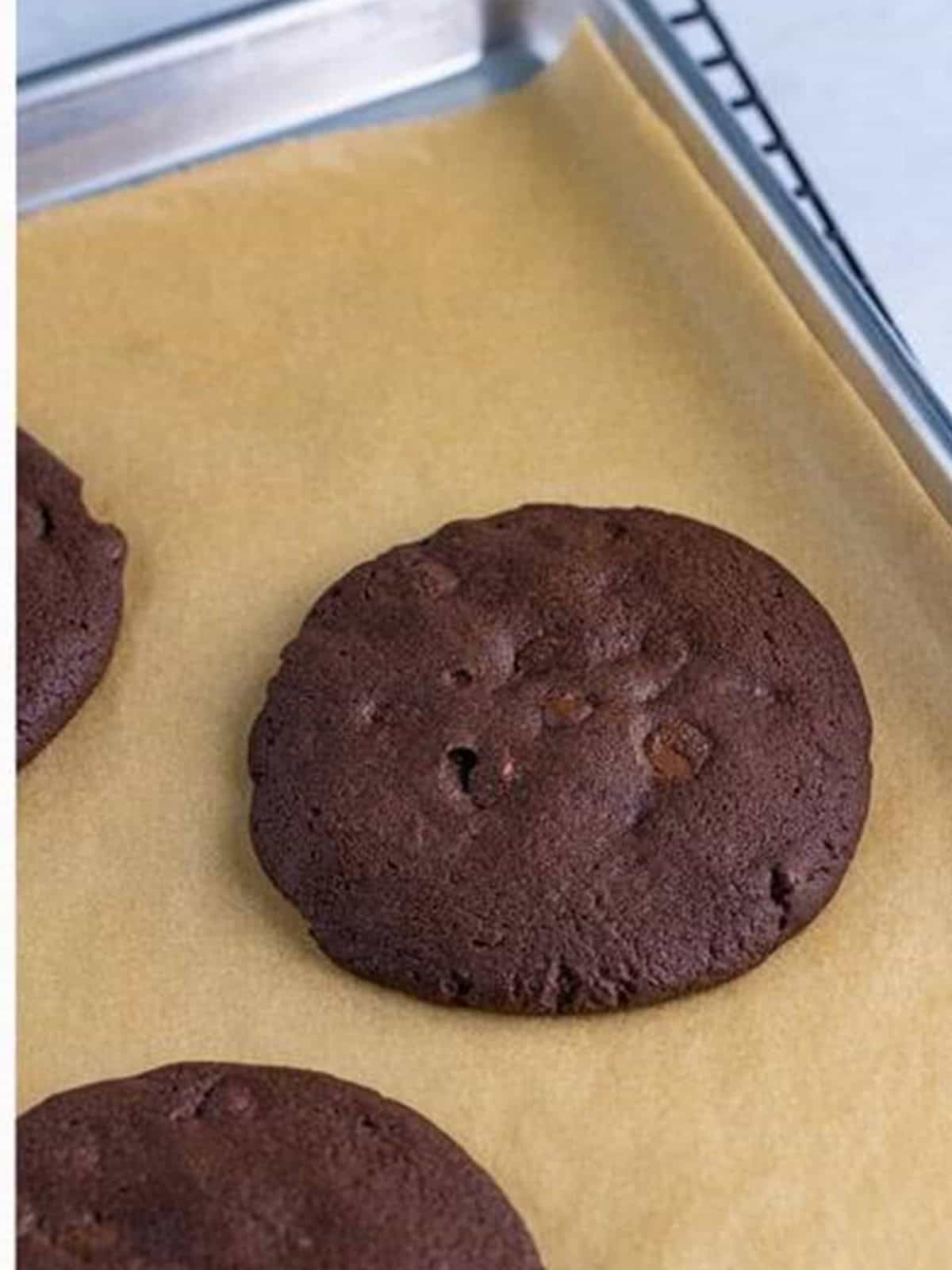 Baked triple chocolate cookies cooling on a sheet tray.
