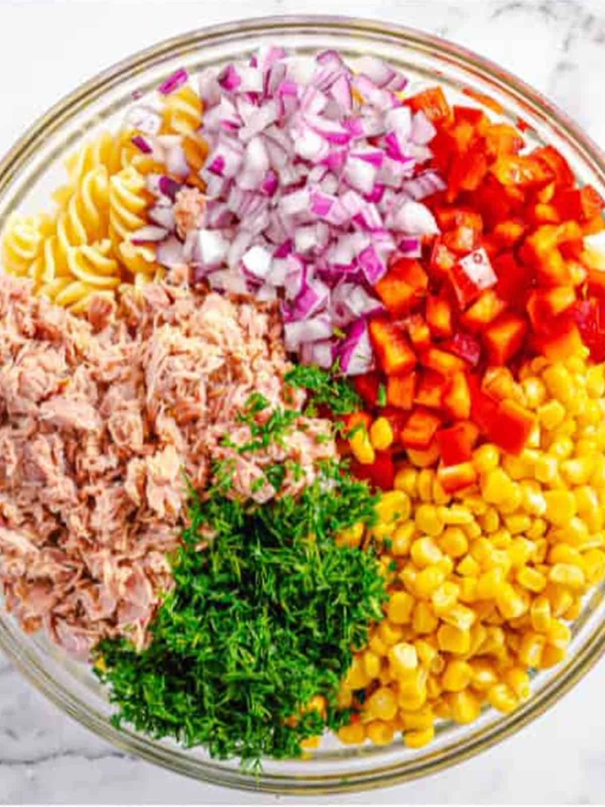 Cooked fusilli, tuna, sweet corn, bell pepper, red onion, and dill added to a large mixing bowl.