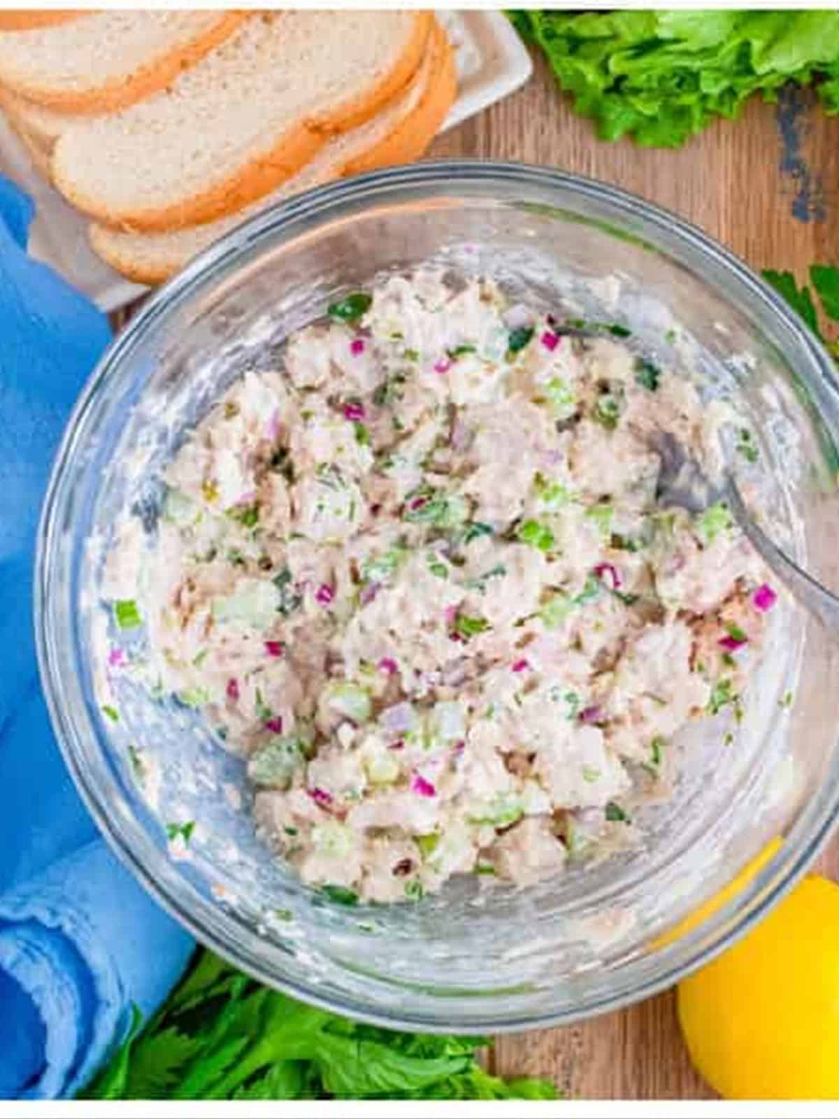Tuna salad mixed together in a glass bowl with celery, onion, and herbs.