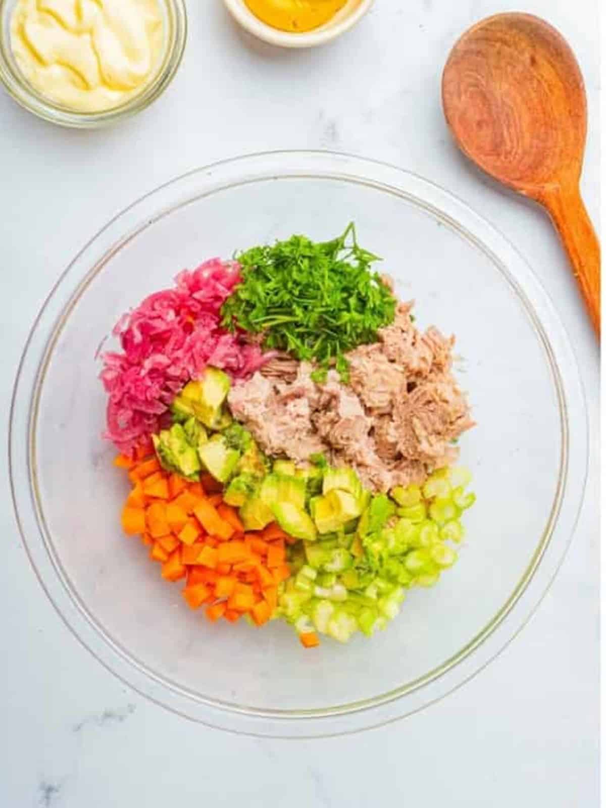 Tuna, celery, carrot, pickled red onion, avocado, and parsley added to a glass bowl for Tuna Salad.
