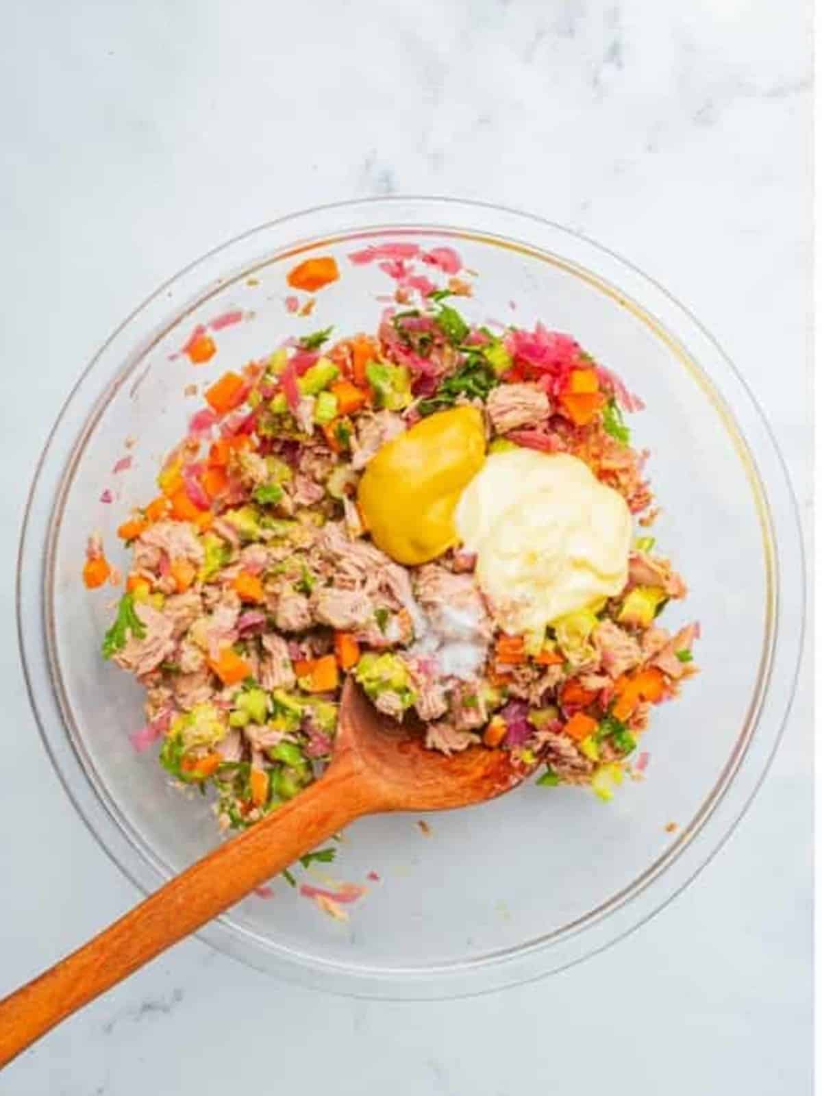 Adding mayonnaise and yellow mustard to the tuna and vegetables for Tuna Salad.