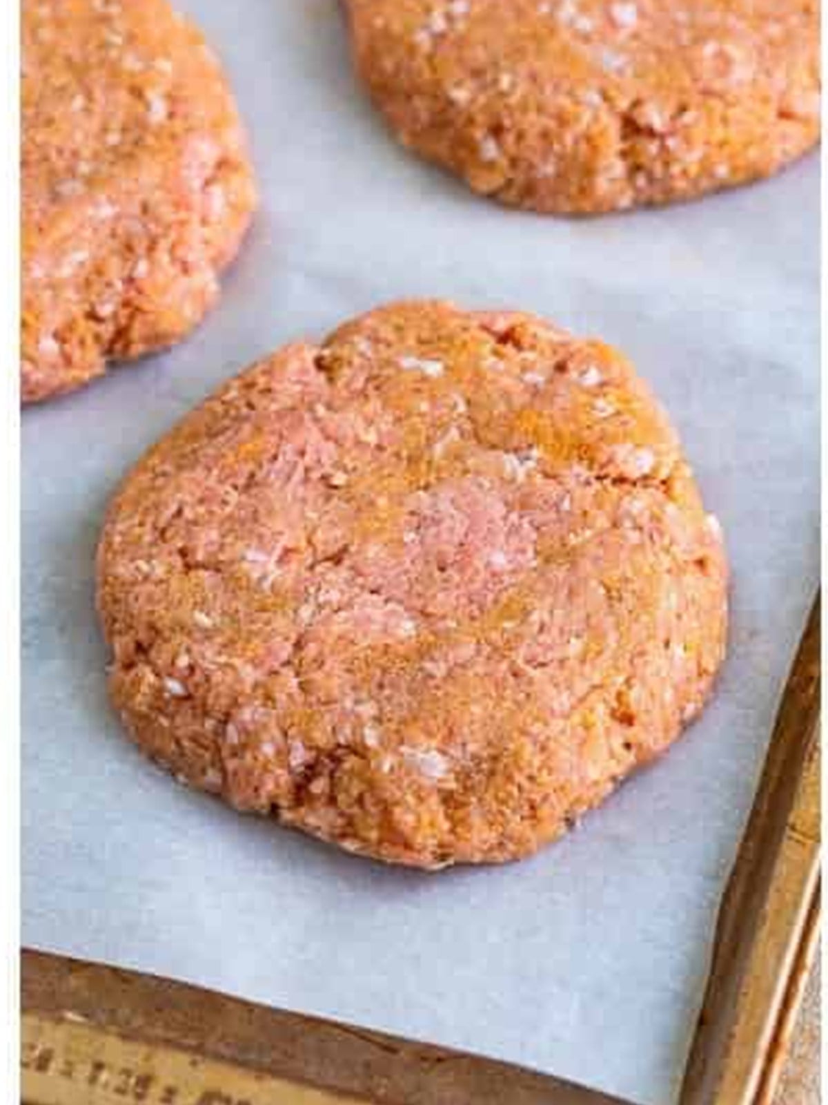 Formed turkey burger patties with a center indentation on a parchment-lined tray.