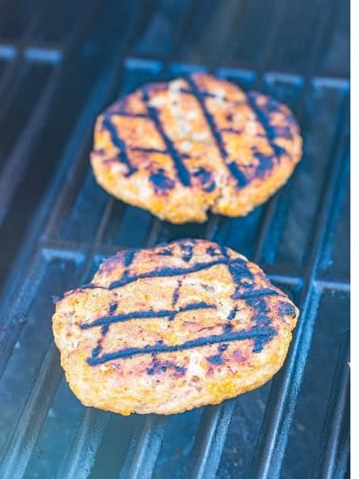 Turkey burger patties cooking with grill marks on a grill.