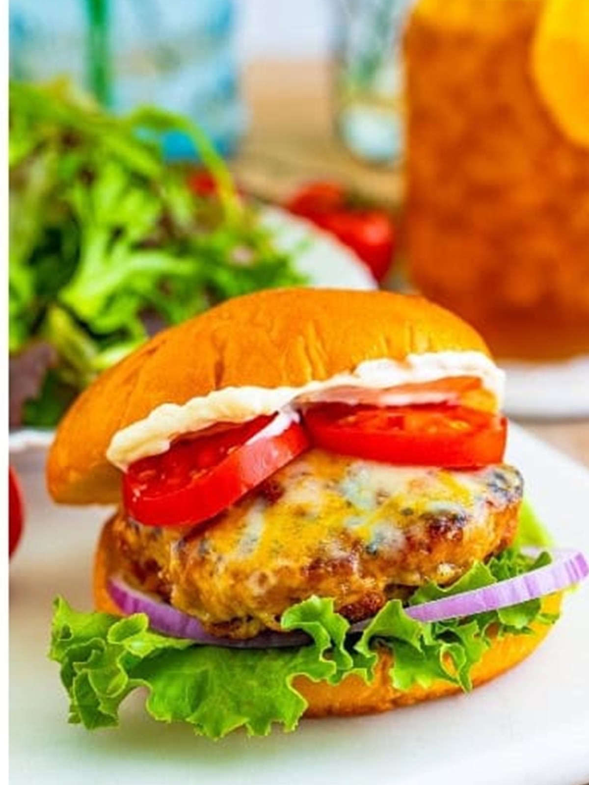 A finished turkey burger on a bun with cheese, lettuce, tomato, and onion.