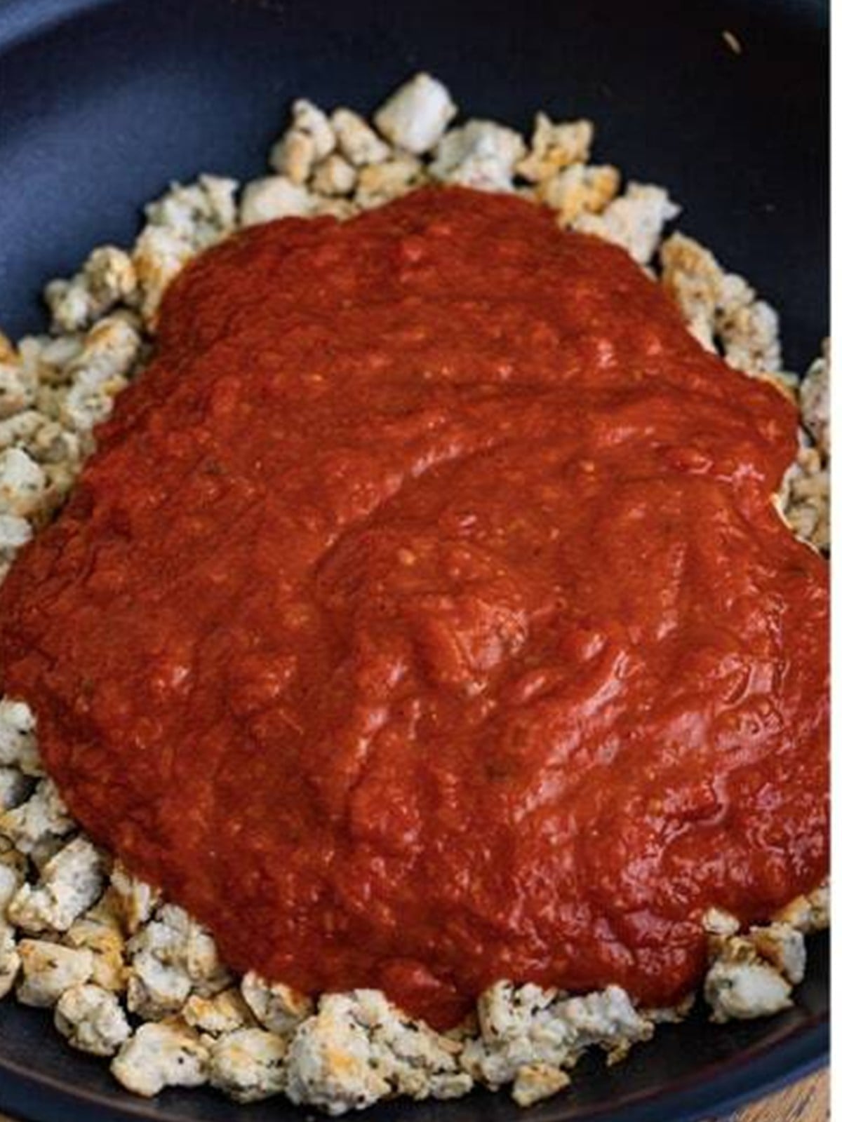 Marinara sauce added to the browned ground turkey in a skillet.