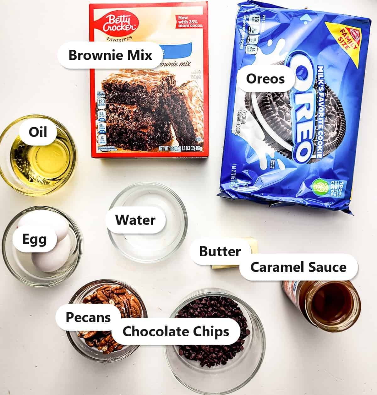 Labeled ingredients for turtle brownie pie including brownie mix, Oreos, pecans, chocolate chips, butter, and caramel sauce.