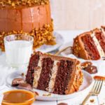 A whole chocolate turtle cake with a slice removed showing the caramel pecan layers.