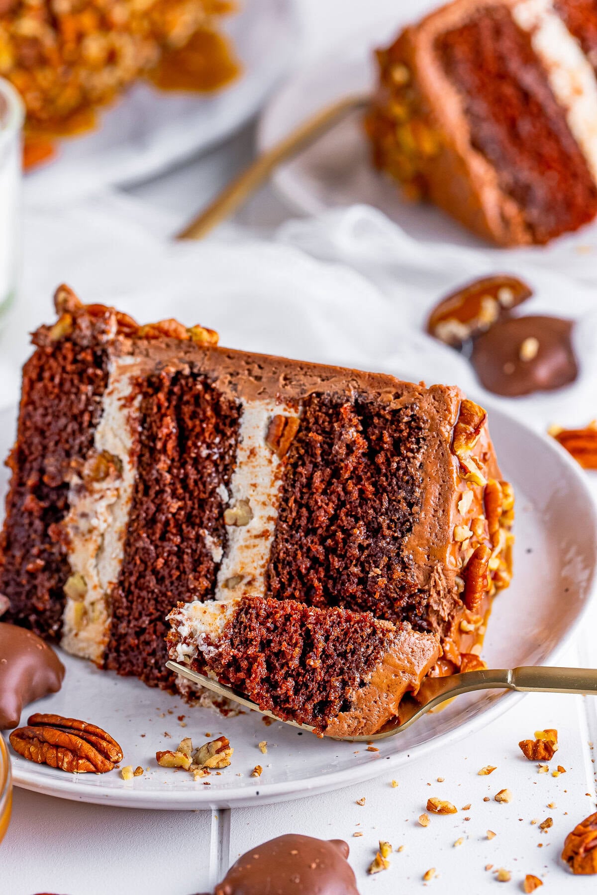 A slice of chocolate turtle cake on a plate showing the caramel pecan filling and chocolate frosting.