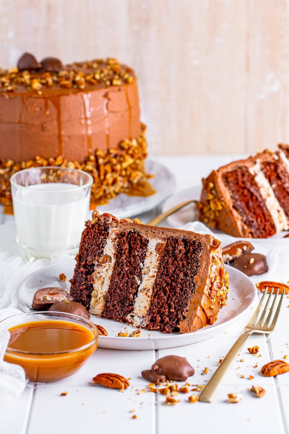 A whole chocolate turtle cake with a slice removed showing the caramel pecan layers.